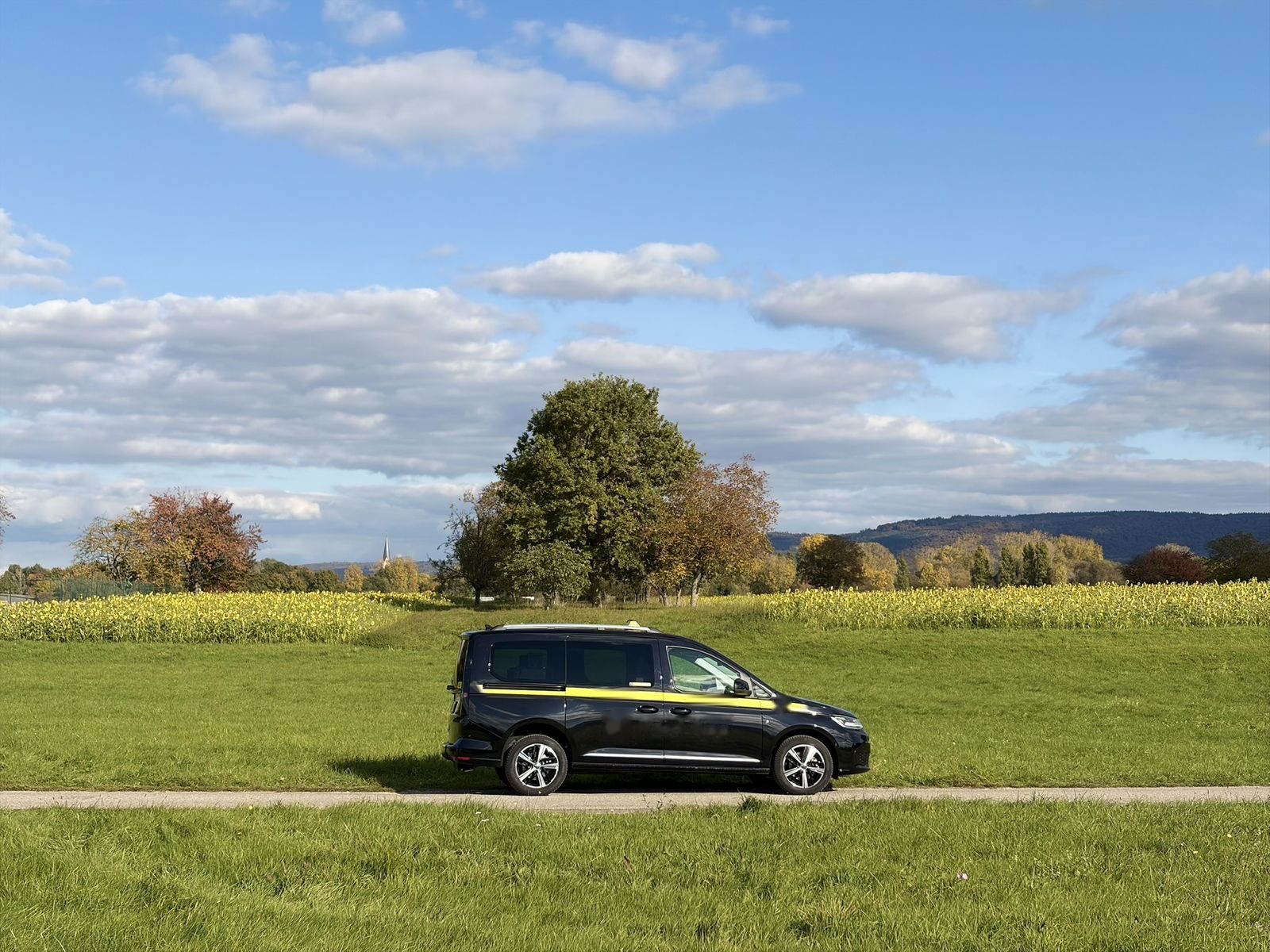 Taxi auf einem Feldweg vor Bäumen und Sonnenblumenfeld